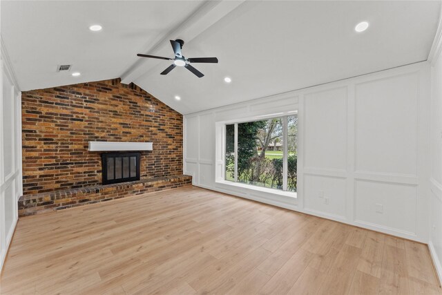 unfurnished living room featuring vaulted ceiling with beams, ceiling fan, light wood-type flooring, a fireplace, and brick wall