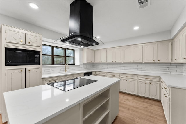 kitchen featuring sink, island range hood, black appliances, light hardwood / wood-style flooring, and backsplash