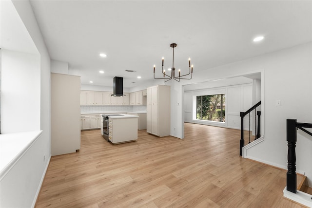 kitchen featuring island exhaust hood, electric range oven, decorative light fixtures, white cabinets, and a kitchen island