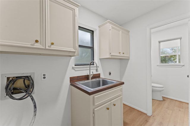 laundry area with hookup for an electric dryer, cabinets, sink, and light hardwood / wood-style flooring