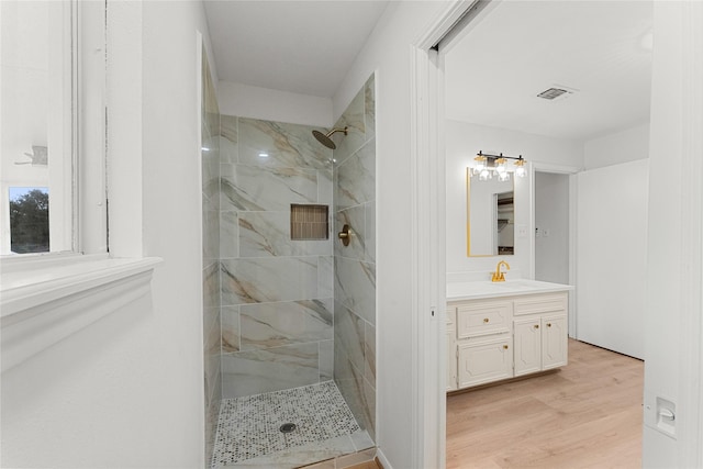 bathroom with hardwood / wood-style floors, vanity, and a tile shower