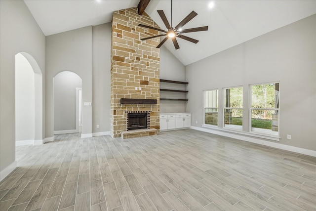 unfurnished living room with baseboards, ceiling fan, beam ceiling, light wood-style flooring, and arched walkways