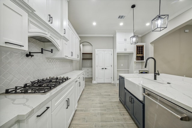 kitchen with pendant lighting, a sink, appliances with stainless steel finishes, white cabinets, and crown molding