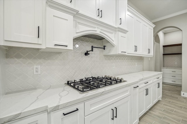 kitchen with backsplash, crown molding, wood tiled floor, stainless steel gas cooktop, and white cabinetry