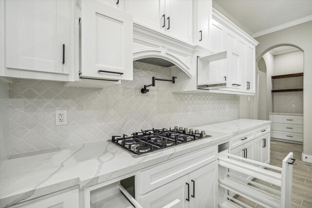 kitchen featuring crown molding, stainless steel gas cooktop, decorative backsplash, arched walkways, and white cabinets