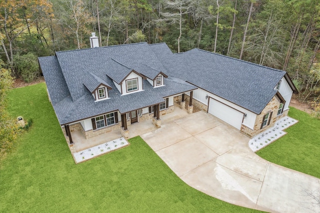 view of front of house with driveway, a porch, a chimney, a front lawn, and stone siding