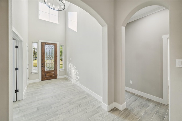 foyer entrance featuring light hardwood / wood-style flooring, a towering ceiling, and an inviting chandelier