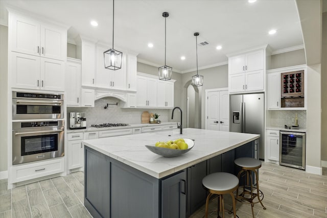 kitchen featuring pendant lighting, light stone counters, white cabinetry, and an island with sink