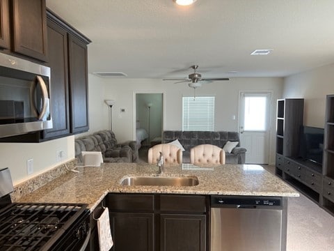 kitchen with light stone countertops, dark brown cabinets, stainless steel appliances, ceiling fan, and sink