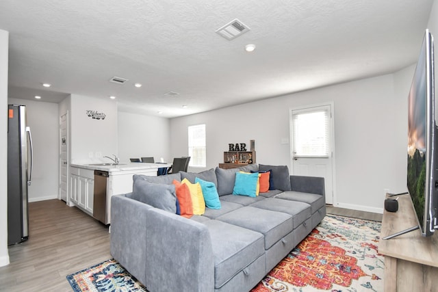 living room with a textured ceiling, sink, light hardwood / wood-style floors, and plenty of natural light