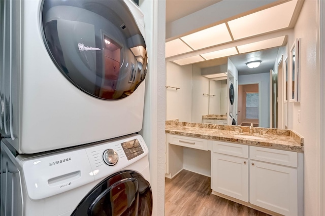 clothes washing area featuring stacked washer / dryer, sink, and light wood-type flooring