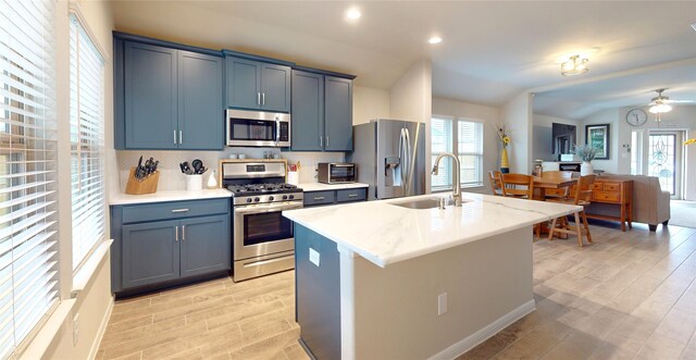 kitchen with stainless steel appliances, sink, backsplash, a kitchen island with sink, and vaulted ceiling