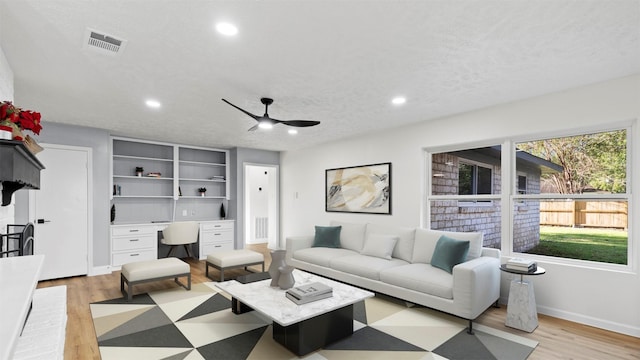 living room with ceiling fan, a textured ceiling, and light hardwood / wood-style flooring