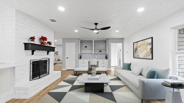 living room with light wood-type flooring, a textured ceiling, a fireplace, and ceiling fan