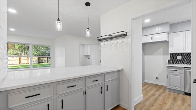 kitchen featuring hanging light fixtures, light stone counters, backsplash, light hardwood / wood-style floors, and a textured ceiling