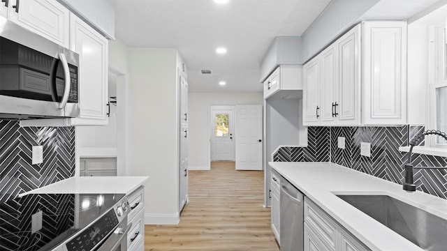 kitchen with white cabinets, appliances with stainless steel finishes, and light hardwood / wood-style flooring