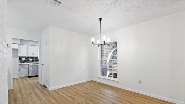 unfurnished dining area featuring a textured ceiling, light hardwood / wood-style flooring, and a notable chandelier