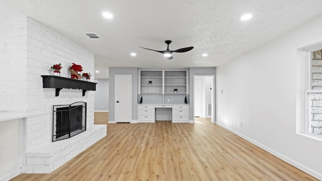 unfurnished living room with a textured ceiling, ceiling fan, built in desk, light hardwood / wood-style flooring, and a fireplace