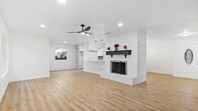 unfurnished living room with a fireplace, a textured ceiling, light hardwood / wood-style flooring, and ceiling fan