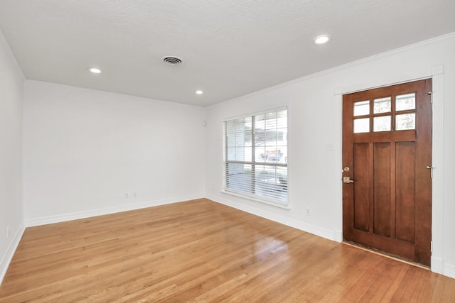 foyer with ornamental molding, a textured ceiling, and light wood-type flooring