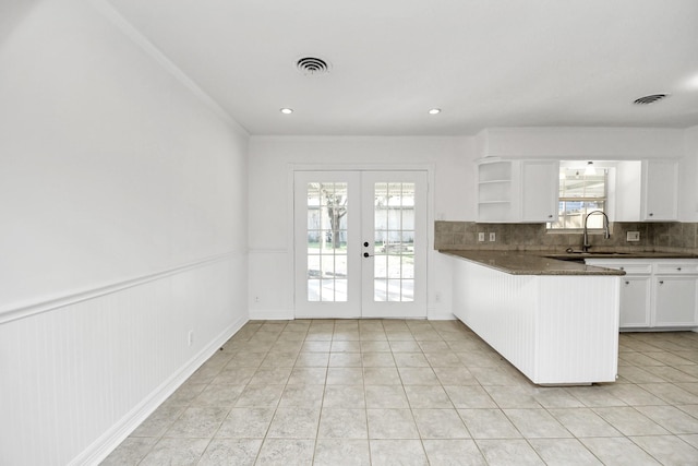 kitchen with sink, white cabinets, dark stone counters, kitchen peninsula, and french doors