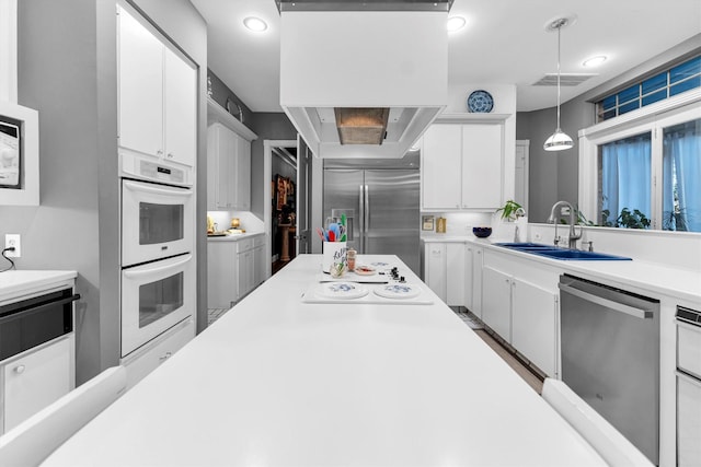 kitchen with stainless steel appliances, sink, white cabinets, and decorative light fixtures