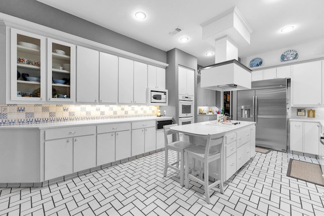 kitchen with backsplash, white appliances, white cabinetry, a kitchen island, and a breakfast bar area