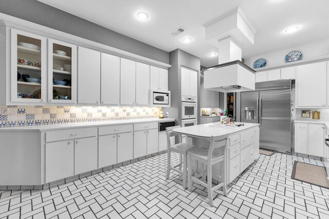 kitchen with a kitchen island, a breakfast bar, tasteful backsplash, white cabinetry, and white appliances