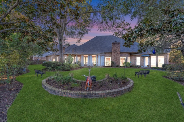 back house at dusk featuring a lawn