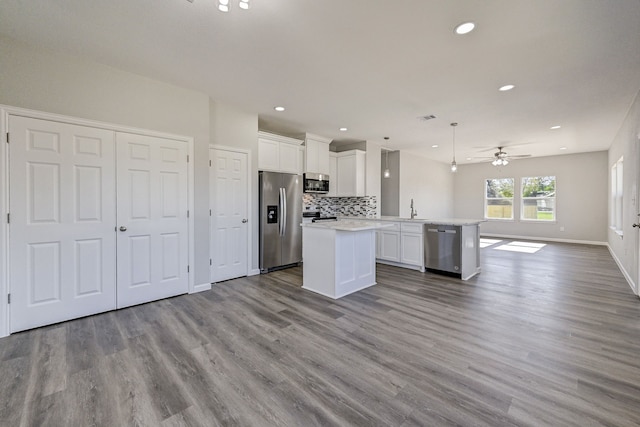 kitchen featuring hanging light fixtures, stainless steel appliances, kitchen peninsula, white cabinets, and light wood-type flooring