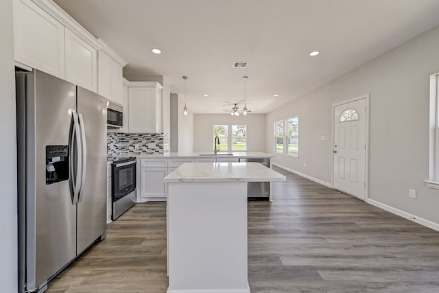 kitchen with kitchen peninsula, stainless steel appliances, decorative light fixtures, white cabinets, and hardwood / wood-style floors