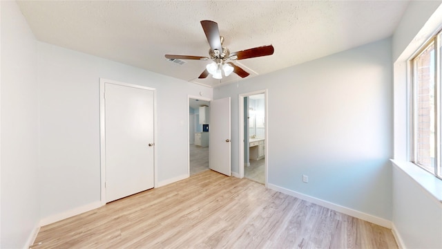 unfurnished bedroom with light wood-type flooring, ensuite bath, multiple windows, and ceiling fan