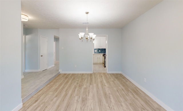 unfurnished dining area with light hardwood / wood-style flooring, a textured ceiling, and an inviting chandelier