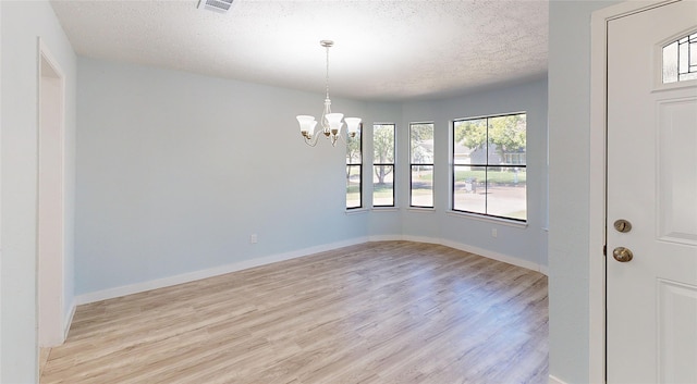 unfurnished room with a textured ceiling, light wood-type flooring, and an inviting chandelier