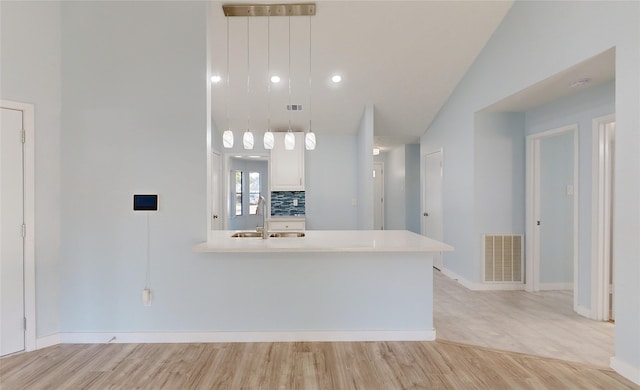 kitchen with white cabinetry, sink, hanging light fixtures, light hardwood / wood-style floors, and lofted ceiling