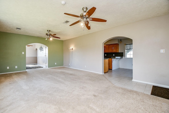 unfurnished living room with light carpet, a textured ceiling, and ceiling fan