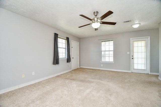 carpeted empty room featuring ceiling fan, plenty of natural light, and a textured ceiling