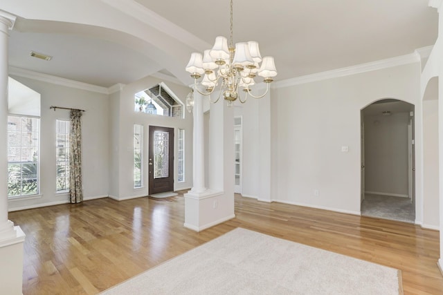 foyer featuring ornate columns, light hardwood / wood-style flooring, a chandelier, vaulted ceiling, and ornamental molding