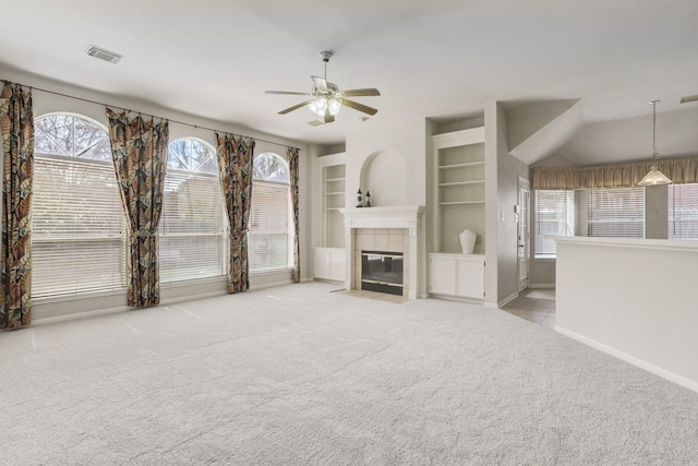 unfurnished living room featuring ceiling fan, light colored carpet, built in features, and a tiled fireplace