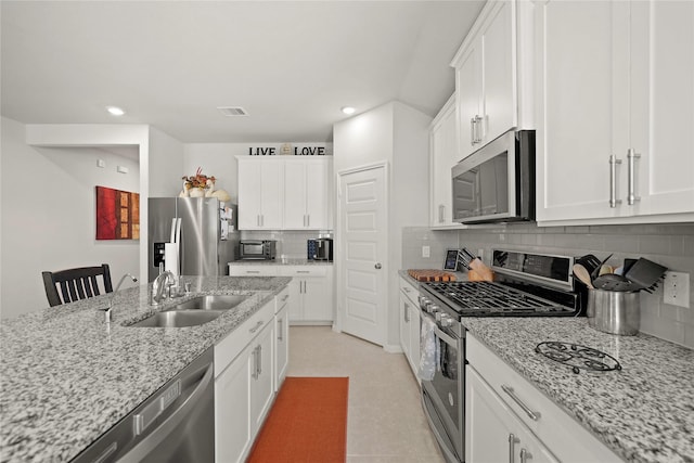 kitchen featuring tasteful backsplash, light stone countertops, white cabinets, and appliances with stainless steel finishes