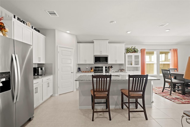 kitchen with white cabinetry, a kitchen island with sink, stainless steel appliances, and light stone counters