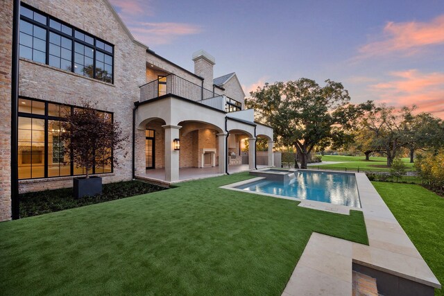 back house at dusk with a lawn, a patio area, and a balcony