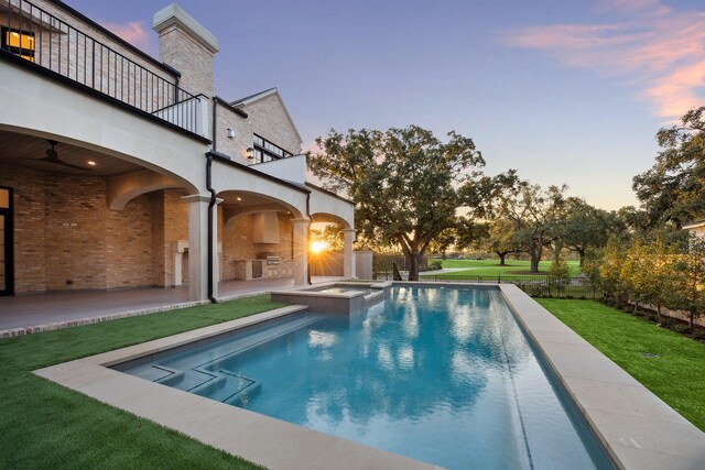 pool at dusk with a lawn, an in ground hot tub, and a patio