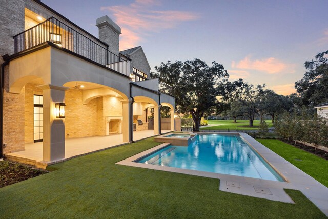 pool at dusk with an in ground hot tub, a patio, and a lawn