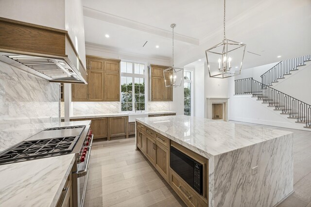 kitchen featuring high end stainless steel range oven, decorative light fixtures, a large island, light stone counters, and black microwave