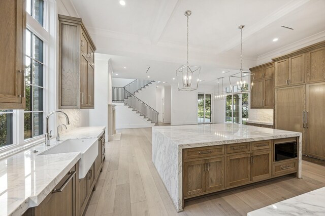 kitchen featuring light stone countertops, light wood-type flooring, black microwave, decorative light fixtures, and a large island