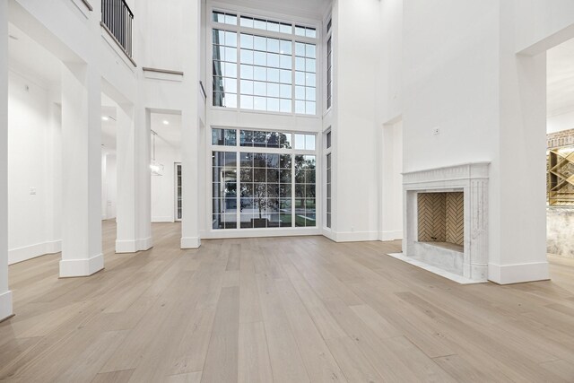 unfurnished living room with a premium fireplace, a towering ceiling, and light hardwood / wood-style floors