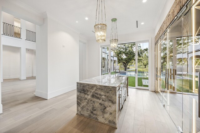 kitchen featuring light stone countertops, a center island with sink, light hardwood / wood-style flooring, a chandelier, and hanging light fixtures