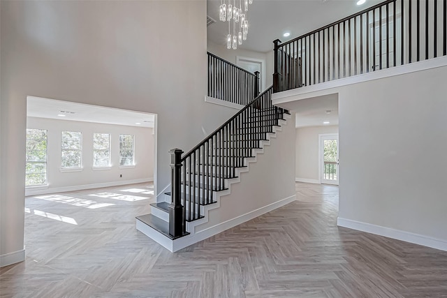 staircase with a towering ceiling, parquet floors, and a notable chandelier