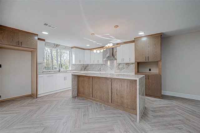 kitchen with white cabinets, sink, wall chimney range hood, and hanging light fixtures